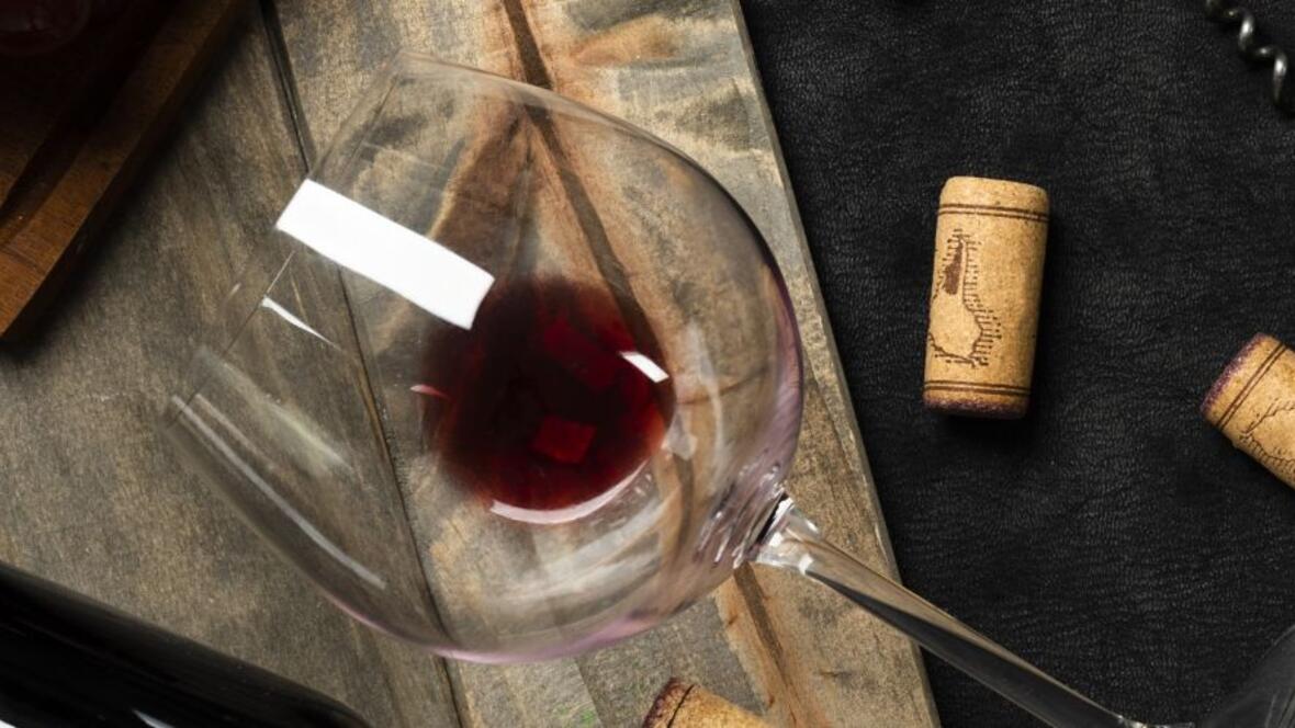 Liegendes Weinglas mit etwas Rotwein auf Holz mit Korken.